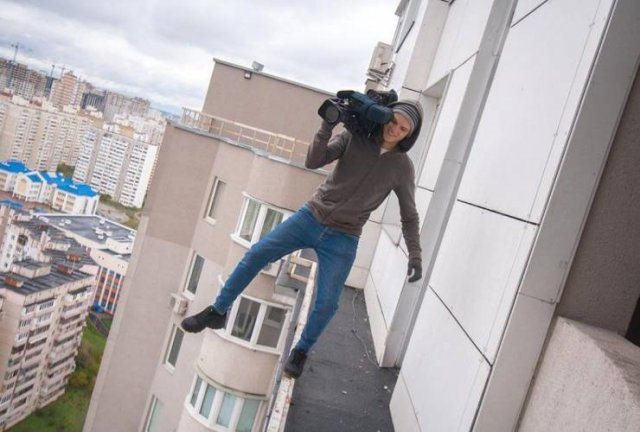 funny pictures of bad ideas, man balancing on the edge of a ledge of a building with a camera