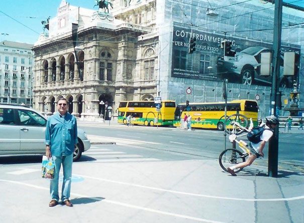 Perfectly-timed photographs, man standing for a photograph as a bicyclist in the background crashed into a pole