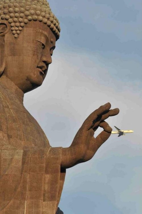 Perfectly-timed-photographs, large statue of buddha with fingers placed over a passing airplane 