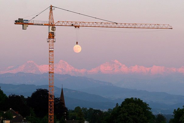 Perfectly-Timed Photograph, crane hovering over outline of the moon in the distance
