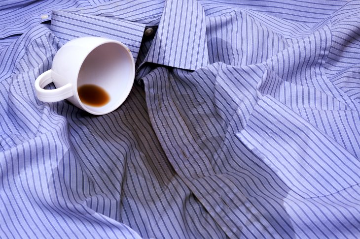 Different coffee stain removal methods, white cup of coffee on its side spilled onto a blue shirt with stripes