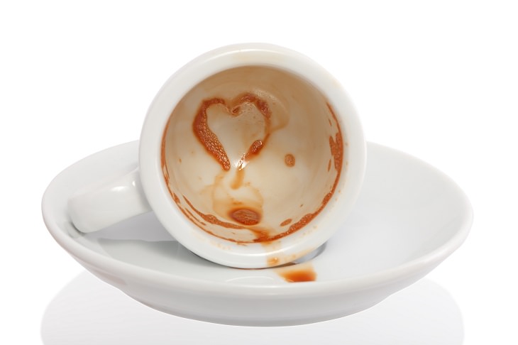 Different coffee stain removal methods, white coffee mug on its side on a white saucer with brown stains inside the mug, one shaped as a heart