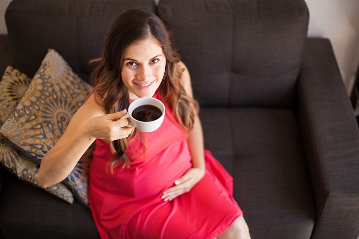 Coffee Stain Removal Methods, Brunette Woman in Pink Dress sitting on a sofa holding a mug of coffee