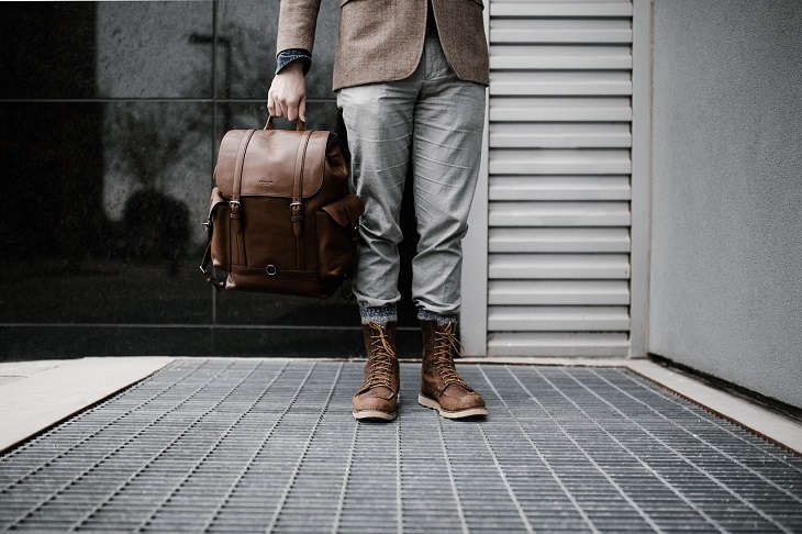Tips for making the most of your next cruise trip, man in coat, jeans and brown shoes holding a small brown backpack 