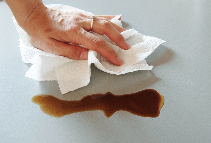 Different coffee stain removal methods, hand with a wedding ring cleaning a coffee stain on a kitchen counter using a white paper towel