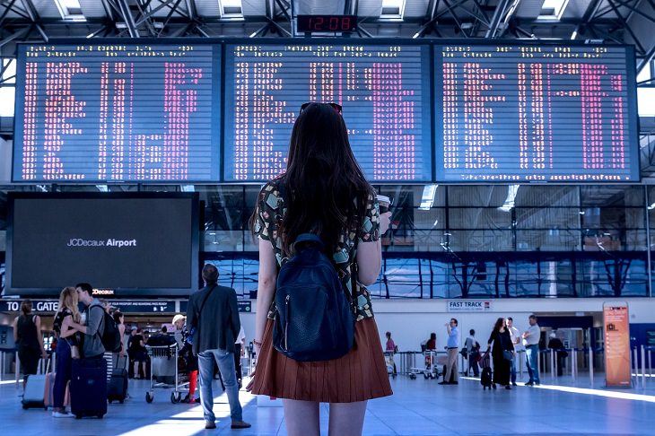 Tips for making the most of your next cruise trip, woman standing in a crowded airport in front of the display board which shows many different flights timings