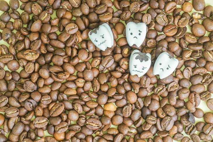 Different coffee stain removal methods, four teeth figurines with sad faces in the middle of a large pile of coffee beans