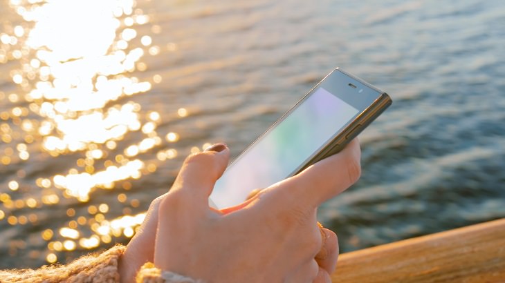 Tips for making the most of your next cruise trip, woman using her phone on the deck of a cruise ship at sunset