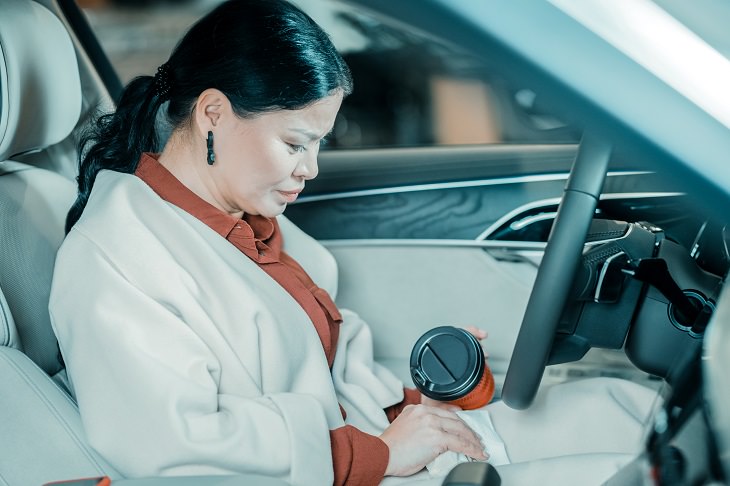 Different Coffee Stain Removal Methods, Brunette woman in a white coat sitting in her car holding a coffee flask 