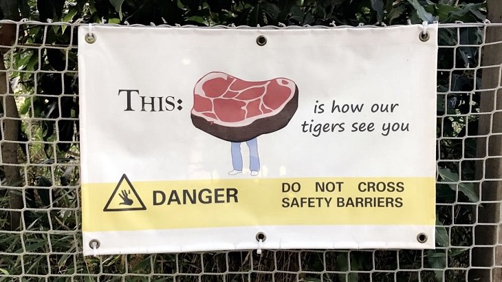 Funny warning and caution signs, warning sign not to cross the border on a fence with a picture of steak with legs stating that that's how tigers see people