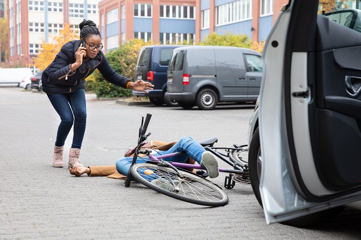 the dutch reach method of opening car doors for safety, woman on the phone calling an ambulance after hit a cyclist with her car door