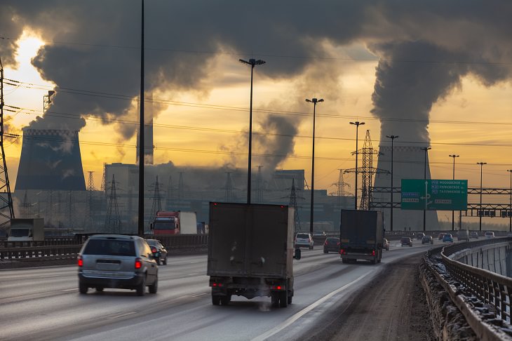 new study reveals air pollution can increase risk of dementia and alzheimer's disease, trucks and cars emitting smoke on a highway, with factories in the background emitting much larger clouds of smoke and pollution