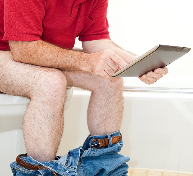 treating the sensation and issue of incomplete bowel movements, man in red t shirt and jeans sitting on a toilet and using his deivice