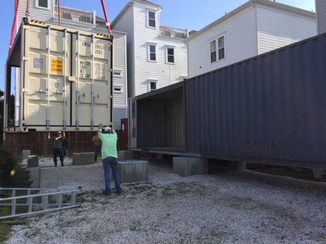 Will Breaux builds a house out of Eleven Shipping Containers, large shipping container in the air next to container placed on the cement piers