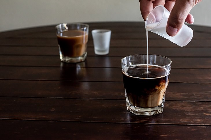DIY homemade coffee creamer, cream being poured from a small glass into a small glass of black coffee