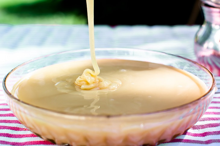 DIY homemade coffee creamer, condensed milk being poured into a bowl outdoors