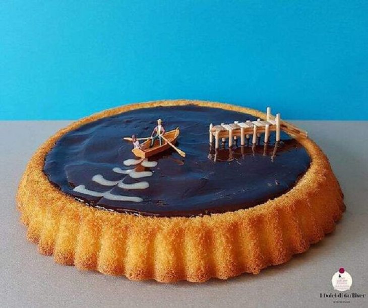 Beautiful Cakes Designed by Italian Chef , Large chocolate tart with miniature figures of two people on a boat with a dock nearby, on the chocolate surface