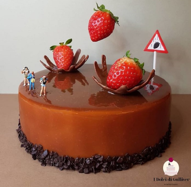 Beautiful Cakes Designed by Italian Chef, Chocolate cake with chocolate chip base and small figurines on it watching as strawberries fall onto the cake with splashes created in chocolate and a warning sign for raining strawberries
