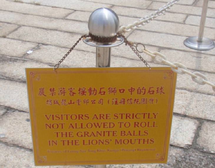 Funny foreign language signs, translations fails, yellow sign chained to a small pole stating Visitors are strictly not allowed to roll the granite balls in the lions mouth