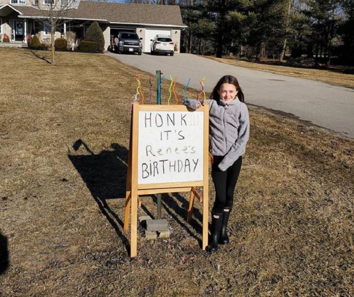 Funny and heartwarming pictures of birthday celebrations during the COVID-19 pandemic quarantine and lockdown, little girl on front lawn standing next to a sign that says “Honk, it’s Renee’s birthday!”