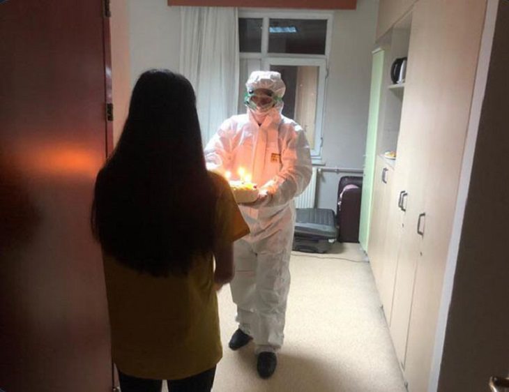 Funny and heartwarming pictures of birthday celebrations during the COVID-19 pandemic quarantine and lockdown, young woman receiving cake from person in full PPE.