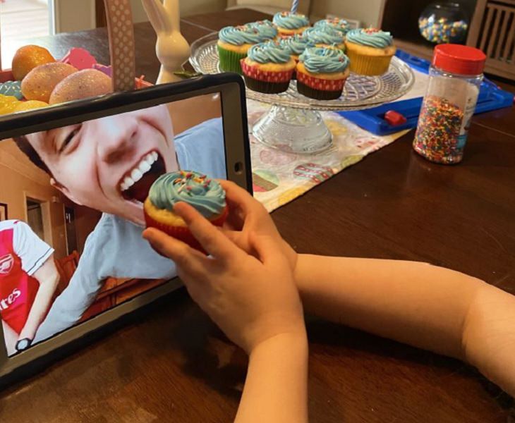 Funny and heartwarming pictures of birthday celebrations during the COVID-19 pandemic quarantine and lockdown, child pretending to feed a cupcake to a man through a video call on an iPad