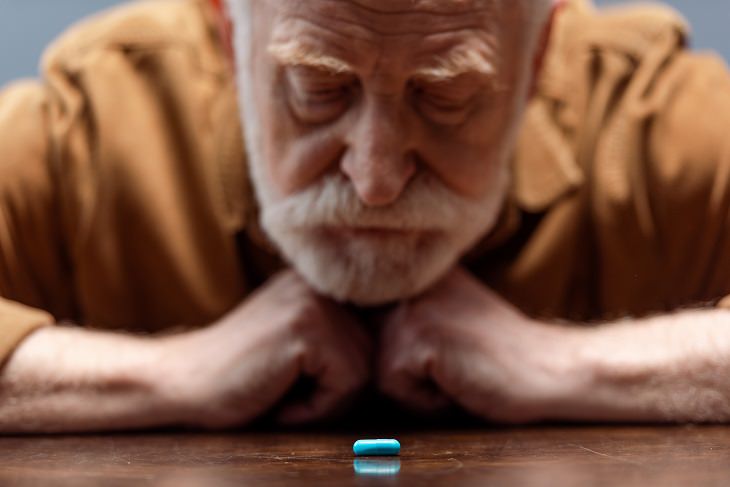 Debunking the myths about mental health, old man with white hair and beard in orange shirt looking at blue pill on table