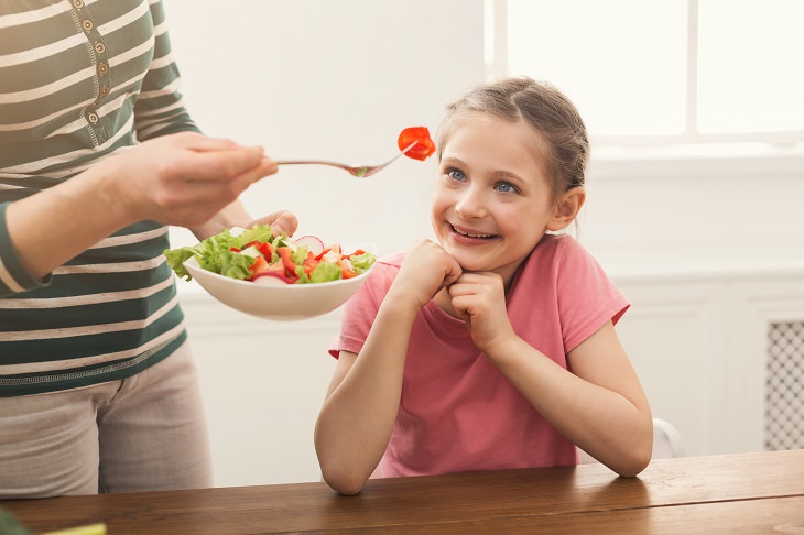 8 tips and tricks to help children develop healthy eating habits, Woman offering her daughter salad