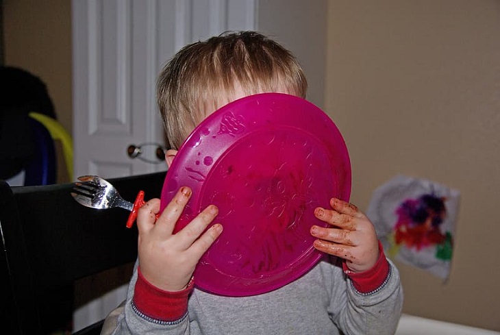 8 tips and tricks to help children develop healthy eating habits, Toddler with messy hands holding pink plate