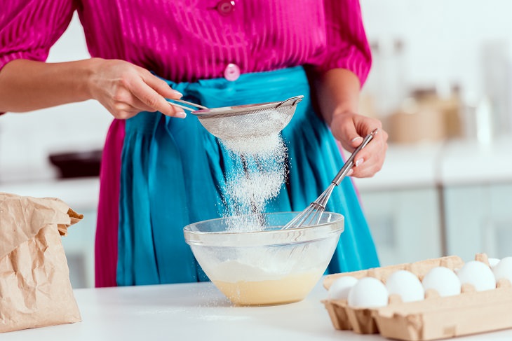 Common cooking mistakes and cooking tips, Partial view of woman in pink and blue sieving or sifting flour to bowl and eggs