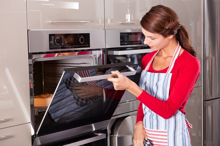 Common cooking mistakes and cooking tips, Woman in red shirt and apron checking the oven
