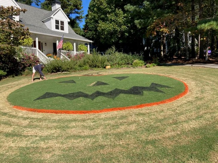 Creative and spooky halloween decorations from 2020, Man working on large grass sculpture of jack-o-lantern face