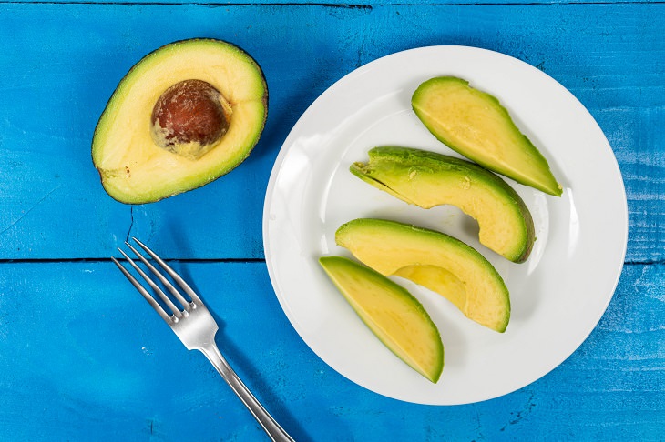 Common ingredients to be avoided in weight-loss smoothies, Sliced avocado on a plate next to half an avocado with a pit in it