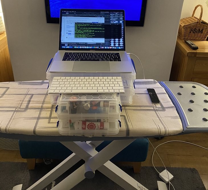 Funny improvised and makeshift work from home (wfh) workspaces and workstations, using boxes of sewing / painting material and ironing table as a laptop desk with keyboard