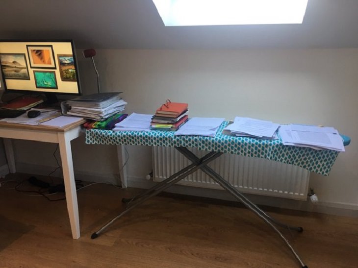 Funny improvised and makeshift work from home (wfh) workspaces and workstations, ironing table covered in piles of documents besides computer table