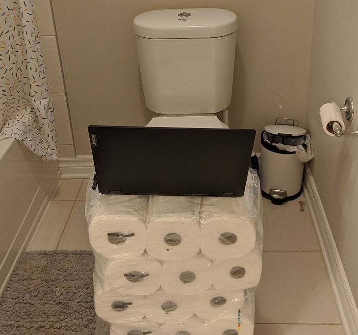 Funny improvised and makeshift work from home (wfh) workspaces and workstations, working in the bathroom with laptop on two bulk packs of toilet paper
