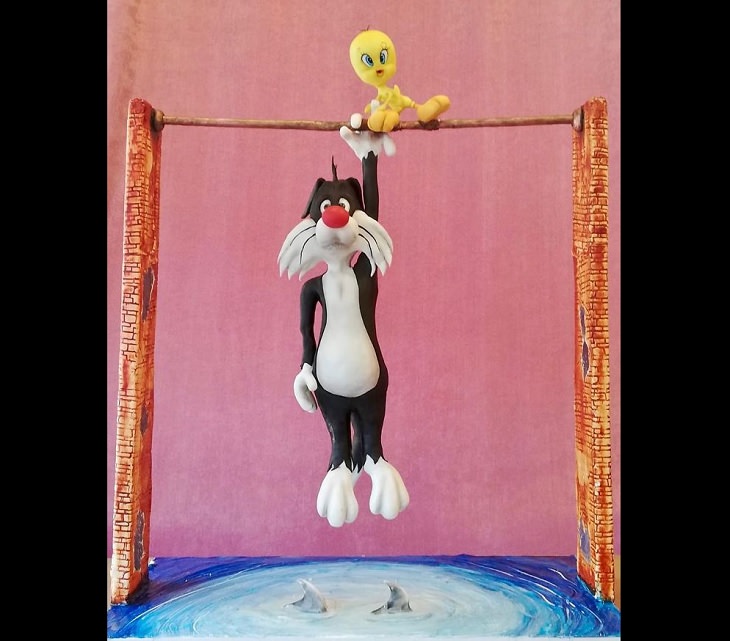 Realistic and Delicious cake art by Turkish chef Tuba Gelick, cake of Sylvester the cat hanging over a pull of sharks while Tweety bird releases his fingers