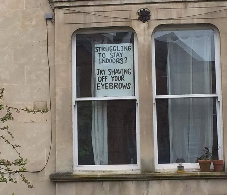 Funny signs related to the quarantine and lockdown caused by the COVID-19 (coronavirus) pandemic, handwritten sign held to window saying “Struggling to stay indoors? Try shaving off your eyebrows.”