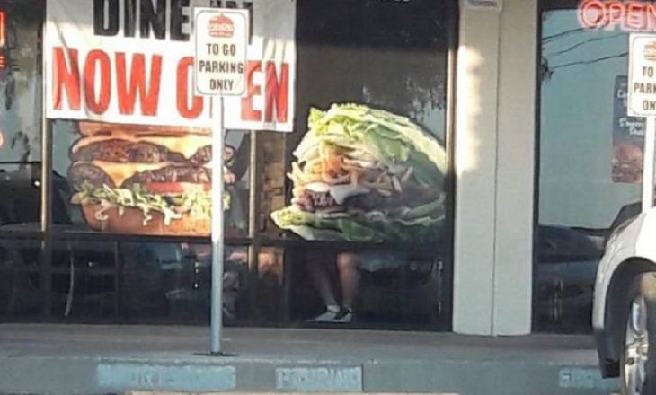 Photographs that will make you look twice or do a double take, Large picture of burger with legs visible of a person sitting in front of it