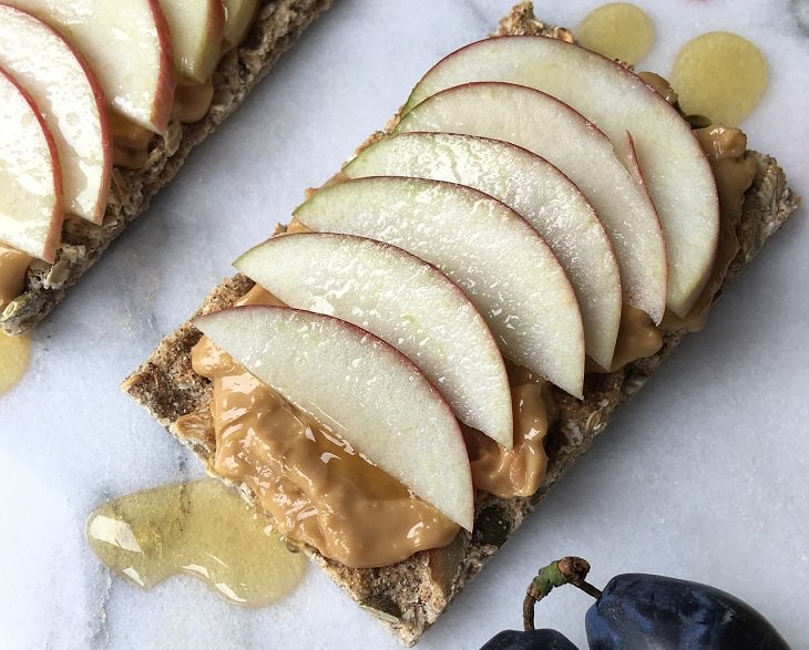 Healthy foods you can enjoy as late-night snacks if you get midnight cravings, Apples and peanut butter on a long slice of bed