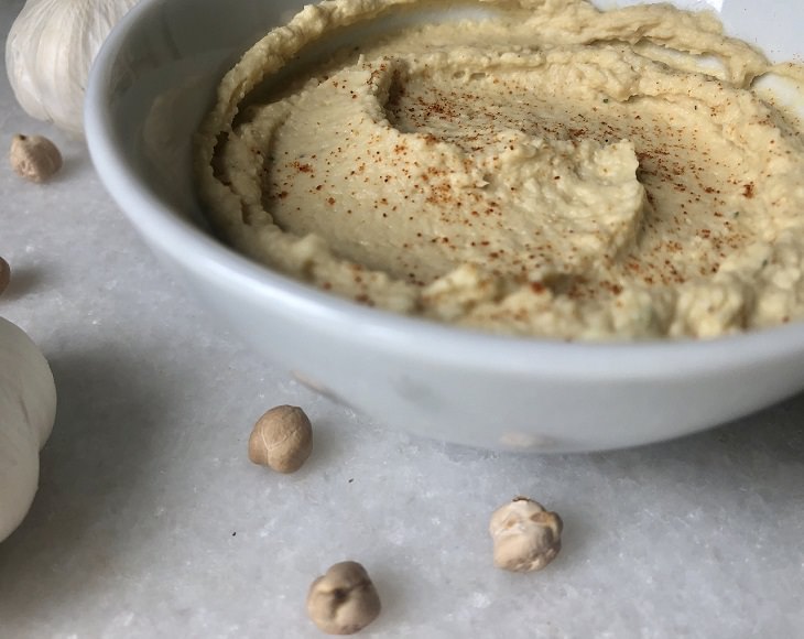 Healthy foods you can enjoy as late-night snacks if you get midnight cravings, Bowl of hummus with a few chickpeas lying beside