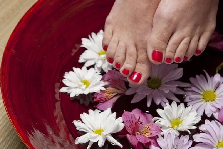 Household uses for old and used teabags, Feet with painted nails about to be immersed in a bowl of liquid, and flowers