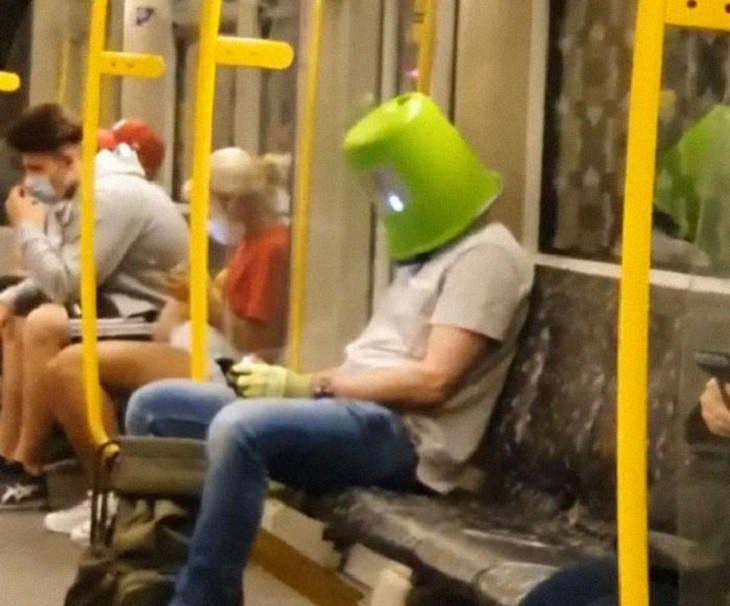 Hilarious photos of strange masks spotted on the subway, Man on subway using his phone wearing a bucket on his head
