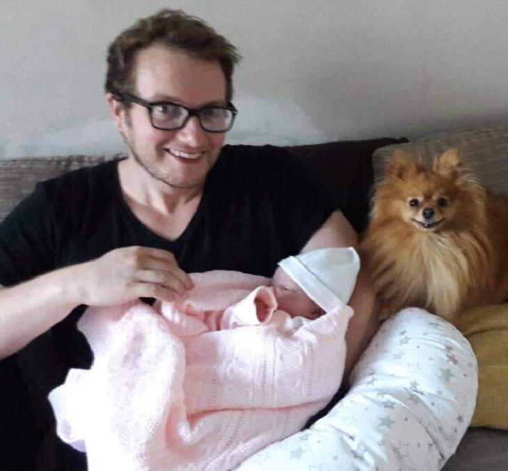 Photographs of smiling dogs, Small brown pomeranian smiling in a photo with a man holding a baby