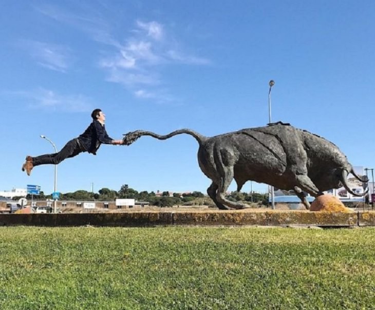 Incredible optical illusions created by Artist and photographer from Portugal Tiago Silva, man holds a statue of a bull by the tail while in the air