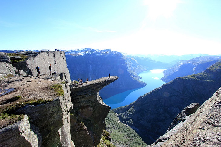 Sights from the popular hiking trail to the rock formation and cliff Trolltunga, near the town of Odda in Norway, Hikers stand on different levels of the cliff