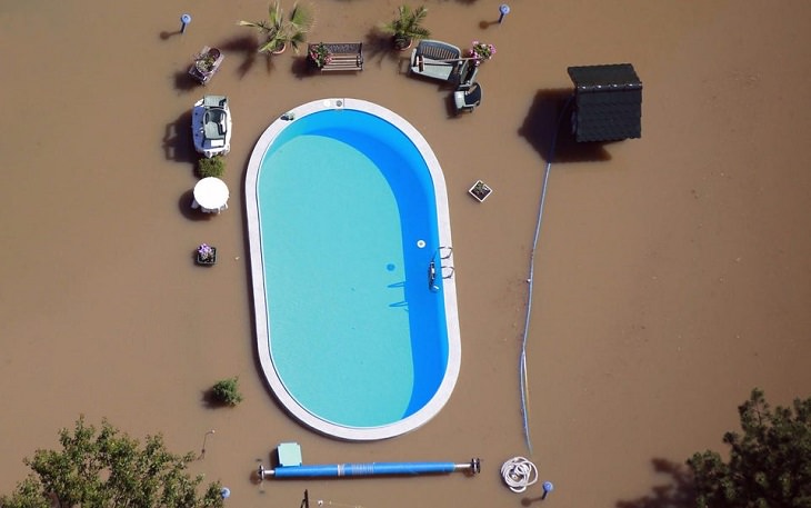 Photos showing the power and aftermath of natural disasters, clean swimming pool untouched by dirty flood water around it