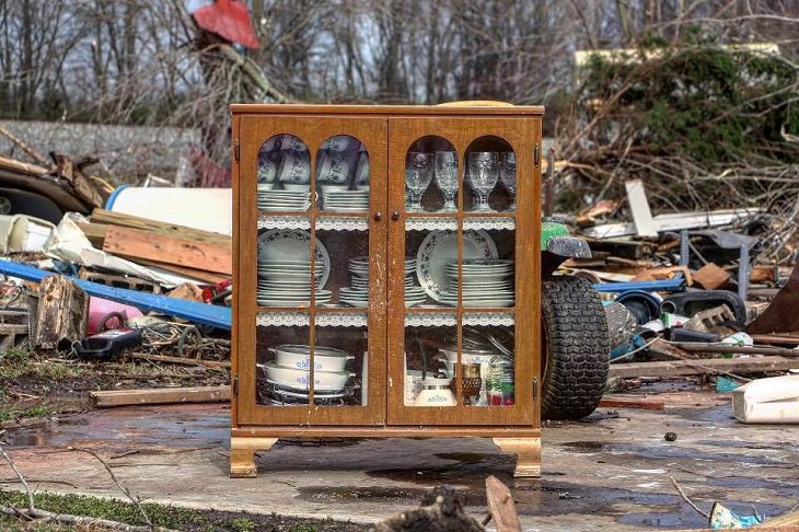 Photos showing the power and aftermath of natural disasters, a china cabinet remains intact while surrounding area is filled with debris after a tornado