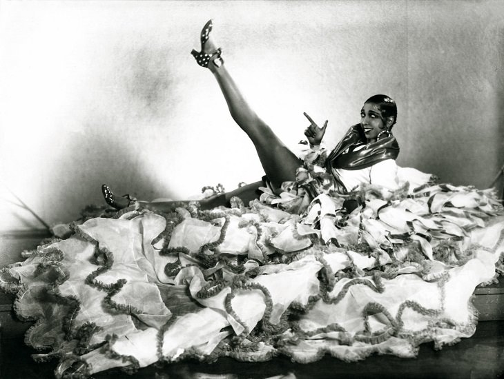 Josephine Baker: Siren of the Resistance, young Josephine Baker lying down in a pile of lace with one bare leg up in the air