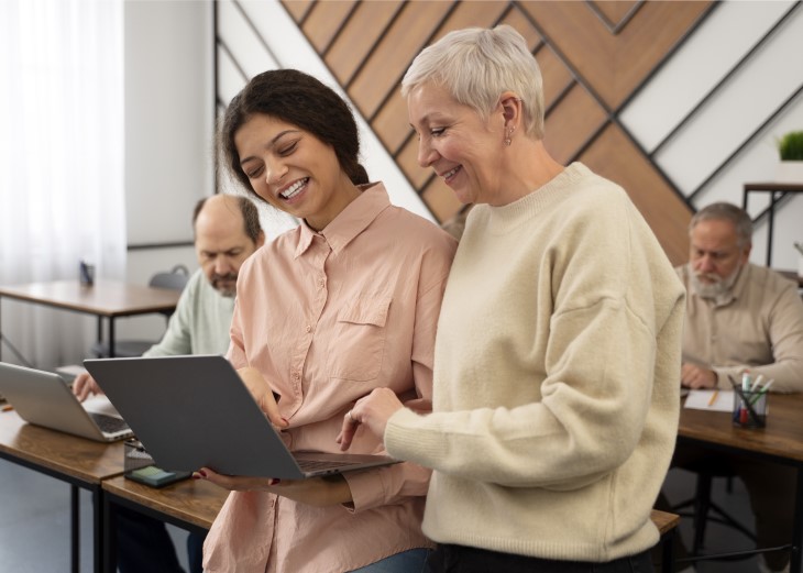 two mature women looking at laptop in a class and smiling